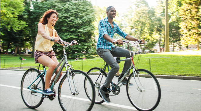 Couple riding bicycles next to a grassy park.